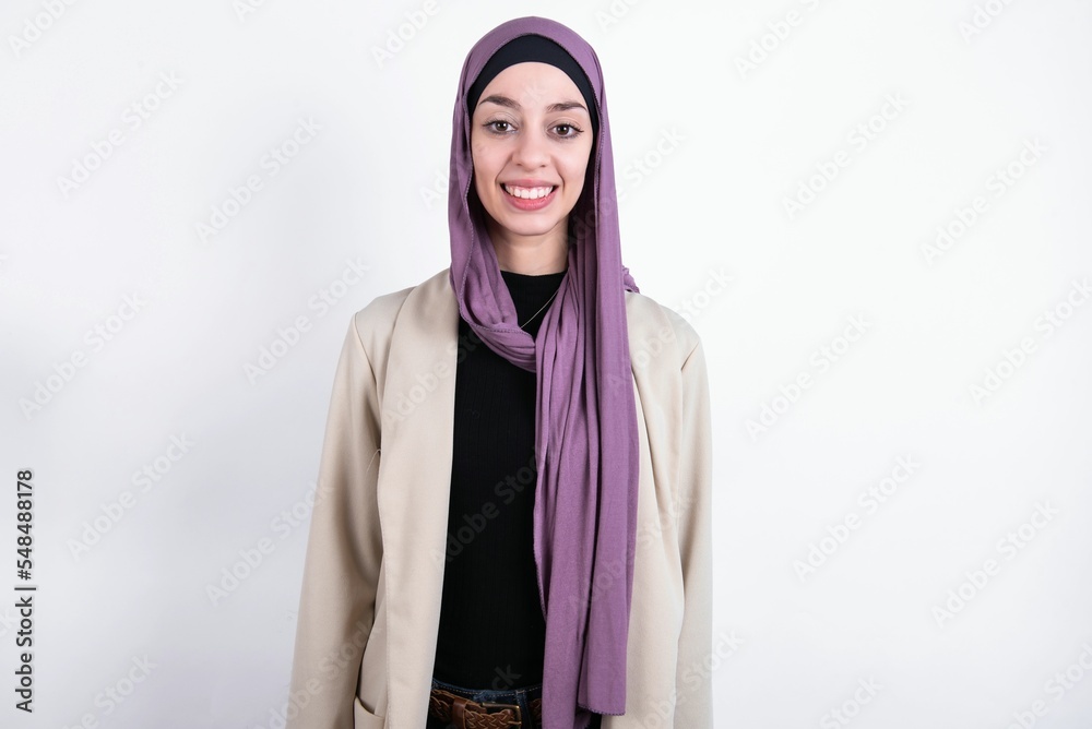 young beautiful muslim woman wearing hijab and jacket over white background with nice beaming smile pleased expression. Positive emotions concept young beautiful muslim woman wearing hijab and jacket over white background with nice beaming smile pleased expression. Positive emotions concept