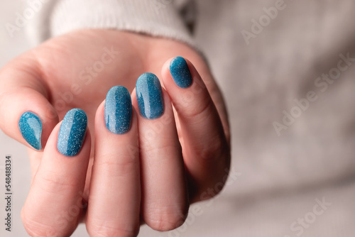 Female hand in gray knitted sweater with beautiful manicure - blue glitter nails. Nail care concept