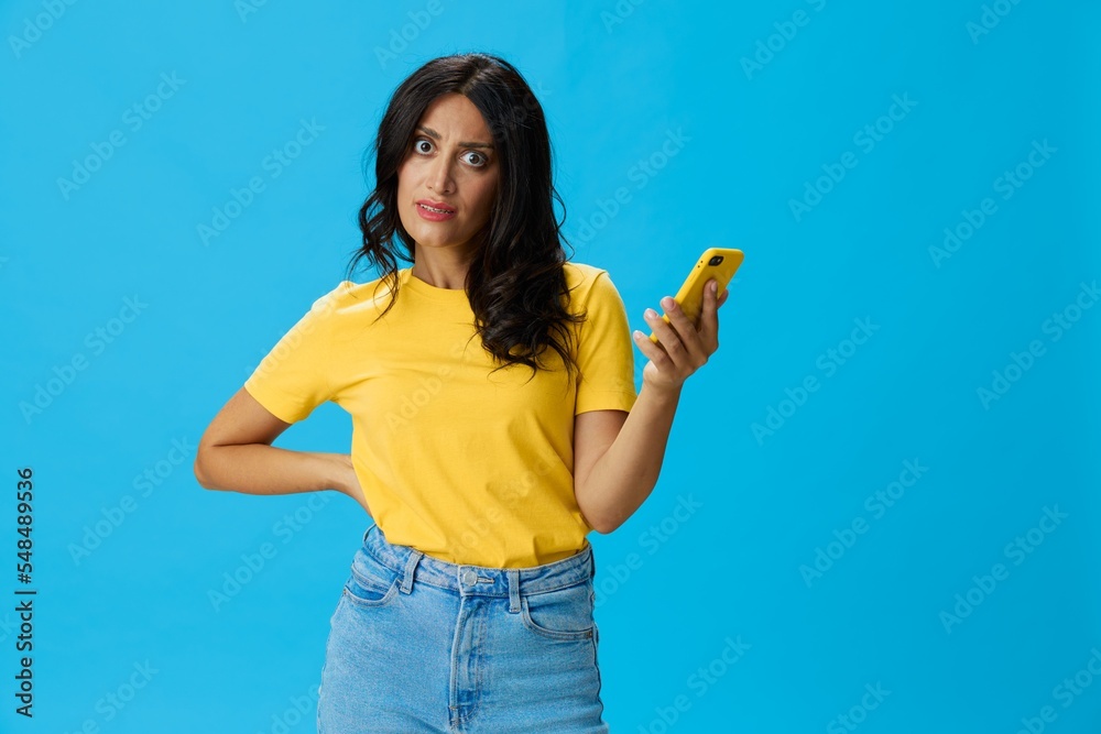 Woman with a phone in her hands with a yellow case on a blue background in a yellow T-shirt, emotions signals gestures, online lifestyle concept, shopping, communication, learning, business online Woman with a phone in her hands with a yellow case on a blue background in a yellow T-shirt, emotions signals gestures, online lifestyle concept, shopping, communication, learning, business online