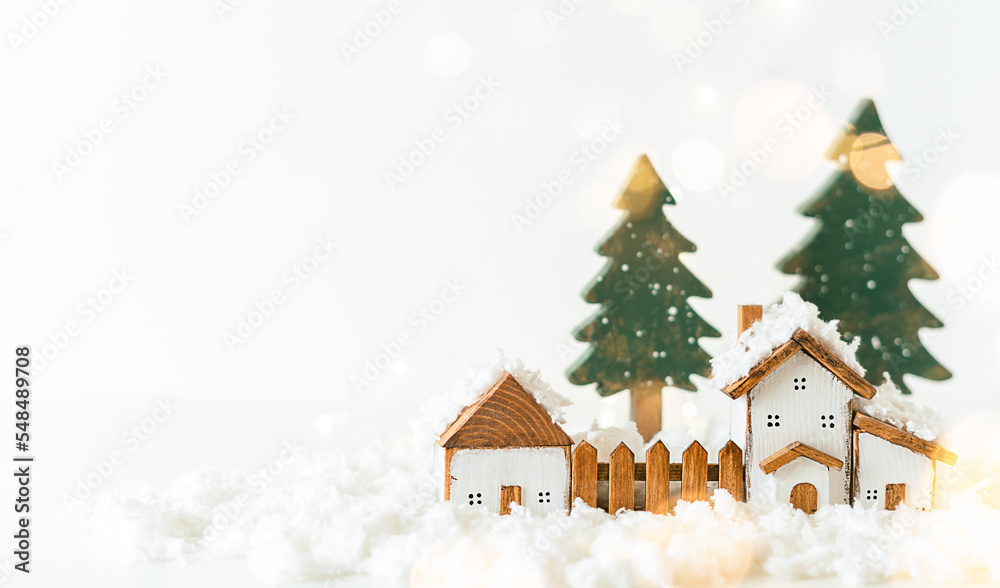 Happy New Year and Merry Christmas postcard. Festive white background with toy wooden house, snow, light bokeh, christmas tree, village and decoration. Copy space for winter holidays greeting card. 