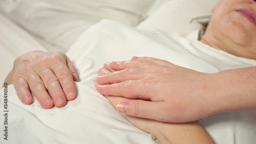 Daughter strokes hand of sick mother lying in bed at home. Woman takes care of elderly bedridden mom after difficult surgery showing support closeup Daughter strokes hand of sick mother lying in bed at home. Woman takes care of elderly bedridden mom after difficult surgery showing support closeup
