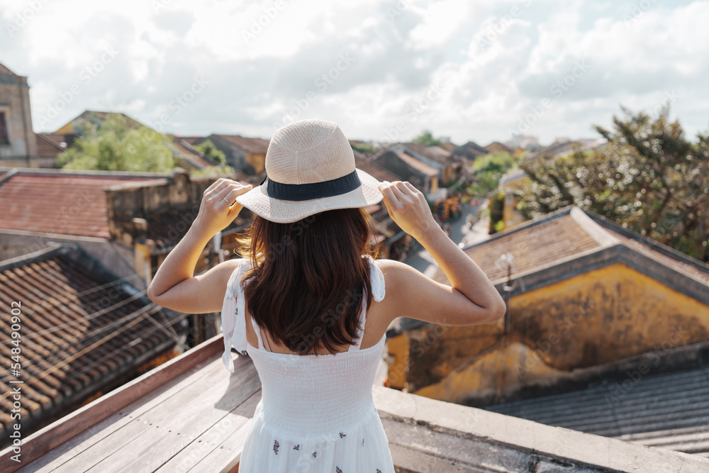 happy traveler traveling at Hoi An ancient town in Vietnam, woman with dress and hat sightseeing view at rooftop.landmark and popular for tourist attractions. Vietnam and Southeast Asia travel concept