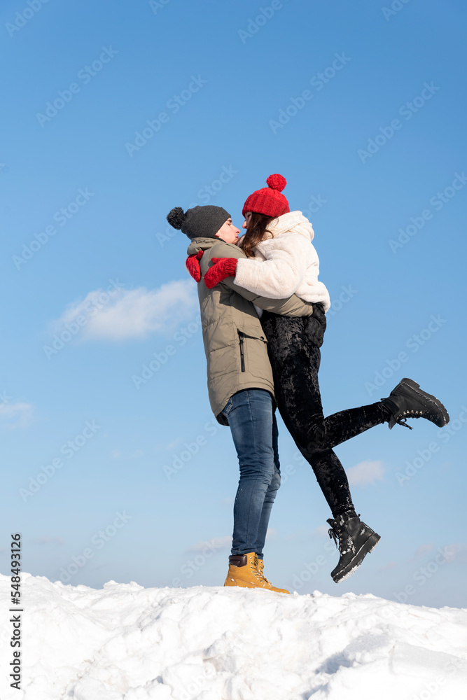 Young couple is walking on winter day. Guy lifted his girlfriend. Portrait of couple in love against blue sky