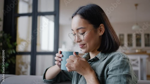 Young Asian woman drinks hot beverage with pleasure at home photo