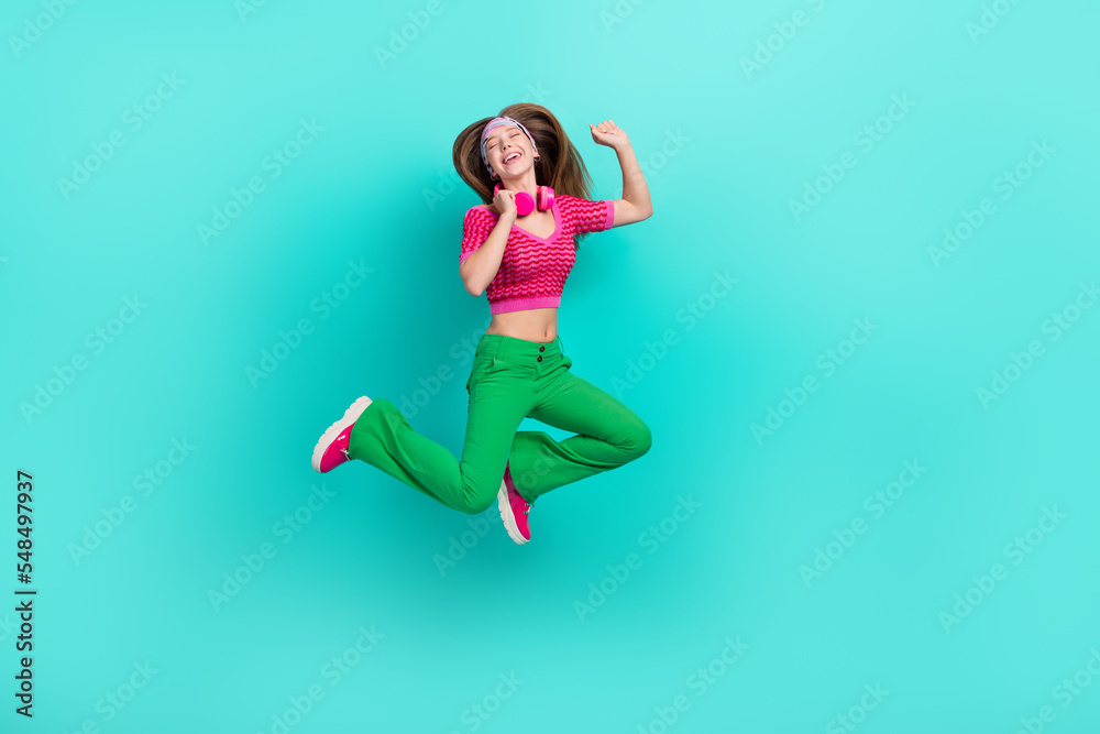 Full length photo of charming dreamy schoolgirl wear pink crop top jumping high listening songs isolated turquoise color background