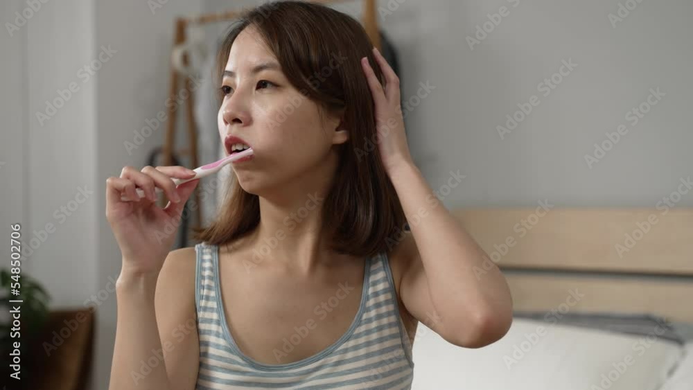 Teenager asian girl brushing teeth while sitting on bed in early morning. lazy woman fell asleep during get ready time with toothbrush. tired female dozy and shocked by dream while prepare in bedroom Teenager asian girl brushing teeth while sitting on bed in early morning. lazy woman fell asleep during get ready time with toothbrush. tired female dozy and shocked by dream while prepare in bedroom