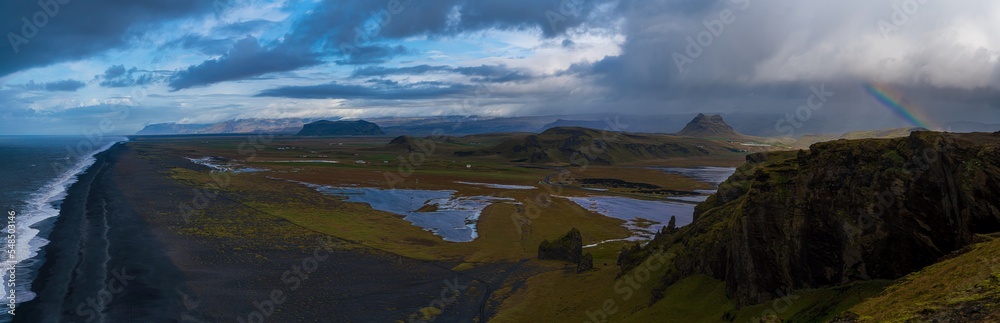 panoramic mountain view of valley and arctic sea under a rainbow rainstorm 