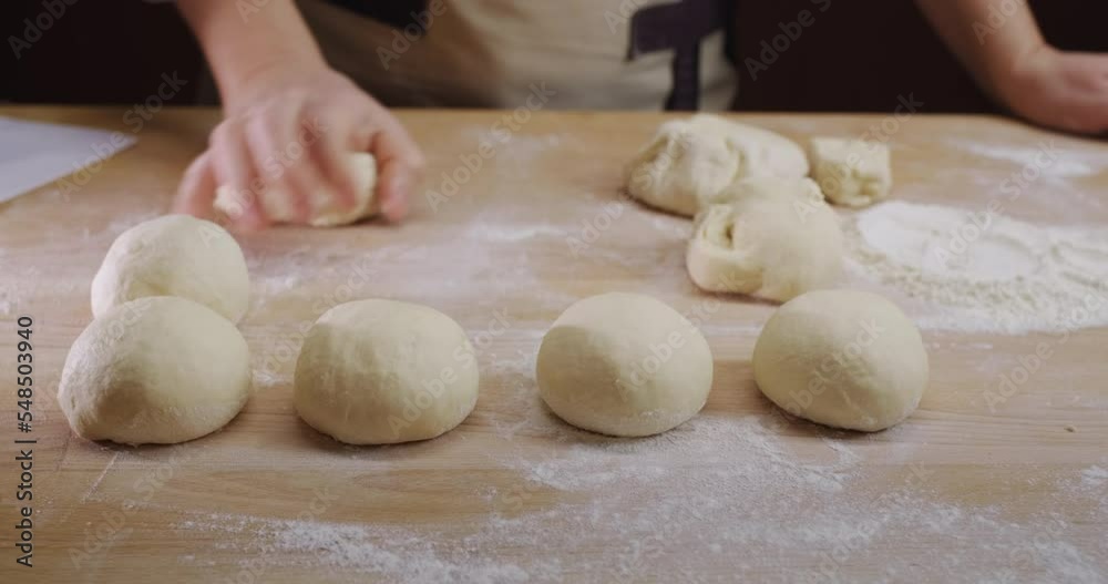 The baker rolls out the dough for buns on the board. Working in a bakery The baker rolls out the dough for buns on the board. Working in a bakery