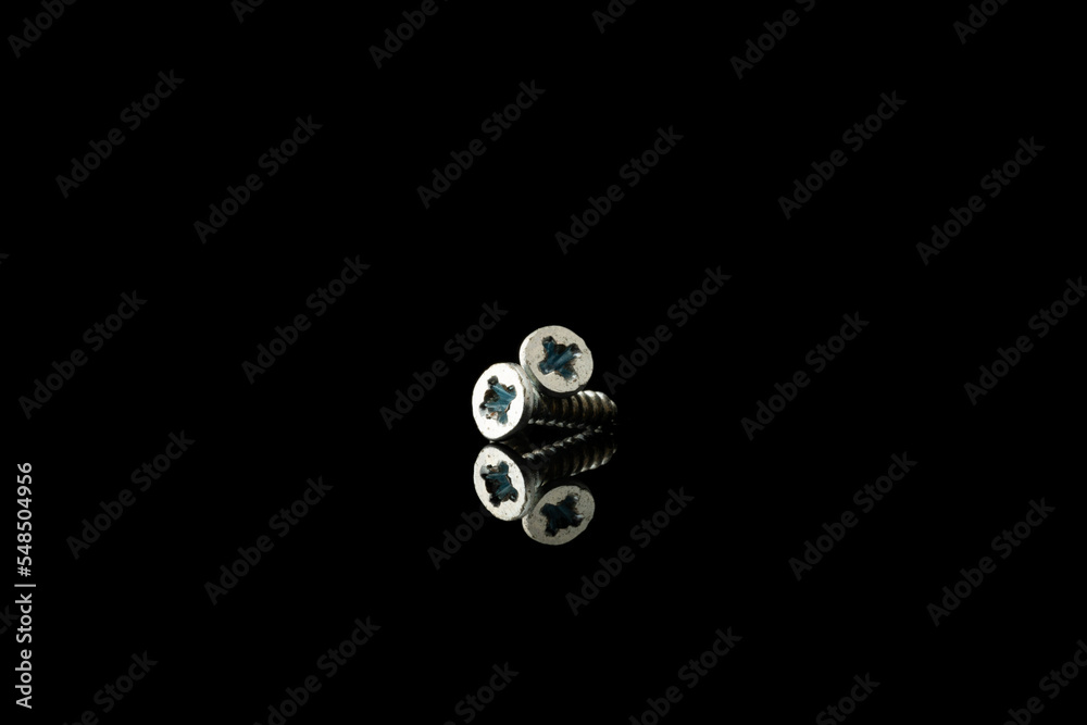 Isolated image of small metal screw in black background with mirror reflection. Isolated image of small metal screw in black background with mirror reflection.