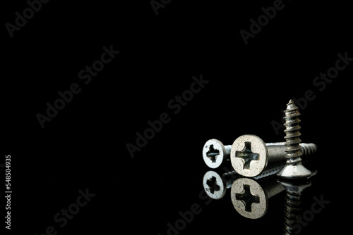 Isolated metal screw on a black plain background cover. Group of phillip head screw with thread on a blank acrylic wallpaper.