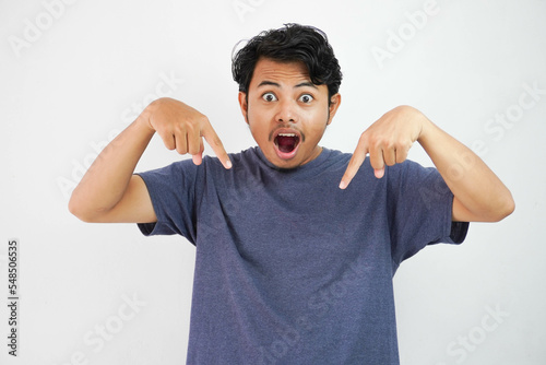Handsome young asian man wearing casual t-shirt amazed and surprised pointing with finger and hand down.