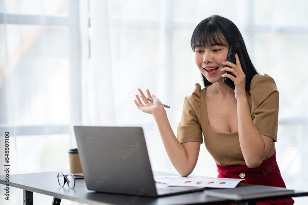 Happy young asian woman talking on the mobile phone and smiling while sitting at her working place in office. Happy young asian woman talking on the mobile phone and smiling while sitting at her working place in office.