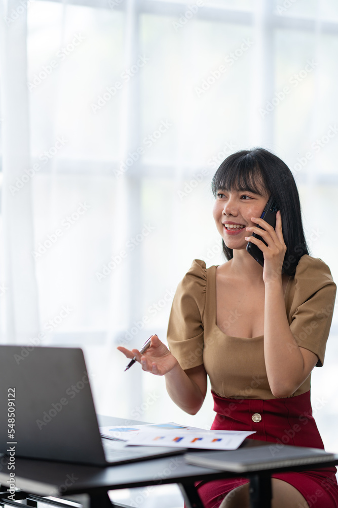 Happy young asian woman talking on the mobile phone and smiling while sitting at her working place in office. Happy young asian woman talking on the mobile phone and smiling while sitting at her working place in office.