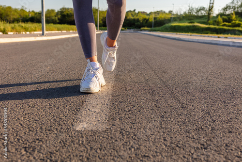 Fototapeta Naklejka Na Ścianę i Meble -  Rearview shot of an unrecognizable young sportswoman's running shoes outside. Woman with running shoes standing on asphalt road.