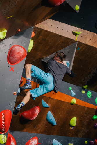 A young, strong guy in a gray T-shirt and blue shorts of athletic build climbs a bouldering in a climbing center at a competition photo