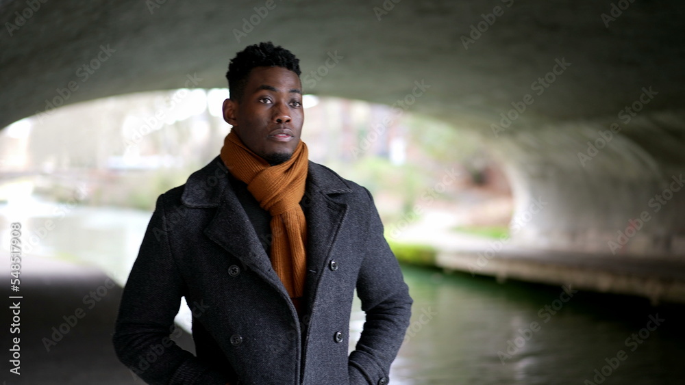 young black man walking under bridge wearing scarf and winter coat young black man walking under bridge wearing scarf and winter coat