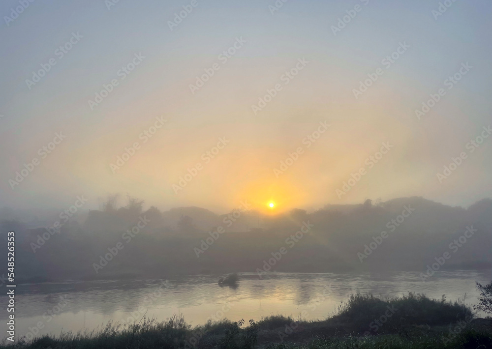 early morning river view the sun rises from the horizon in the east. Soft golden yellow sunlight hits the fog and steam. Soft and selective focus