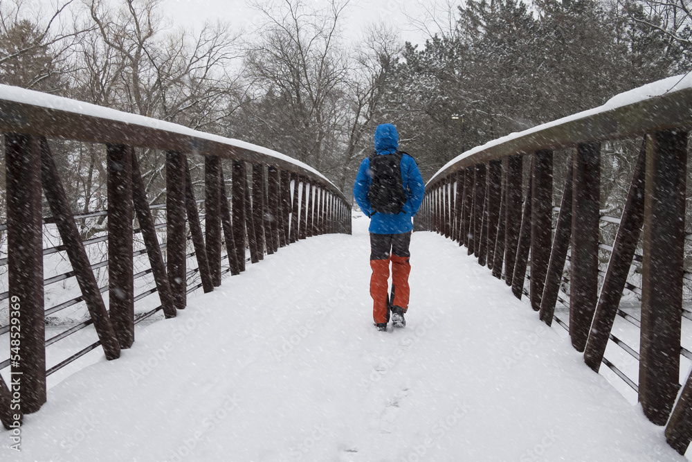 Man in a winter sports clothes walking on a bridge in city park during heavy snowstorm in Toronto, Ontario. Active weather, severe conditions, cold and snowstorm warning concept.