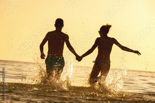 Happy young couple runs at sunset sea beach