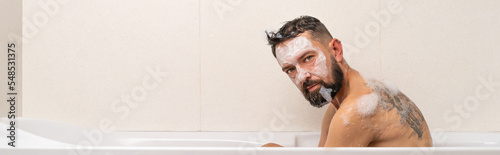 Bearded man with mask on face looking directky in camera while relaxing in bath at home