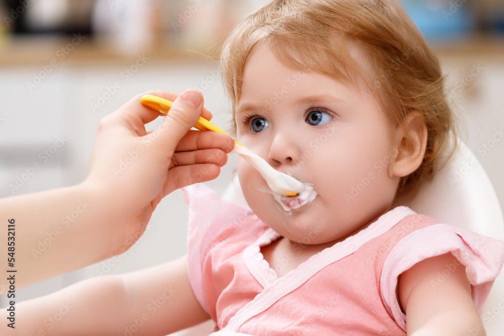 feeds baby with a spoon porridge. A little girl eats food himself sitting on a high chair. A child kid has a good appetite, healthy eating feeds baby with a spoon porridge. A little girl eats food himself sitting on a high chair. A child kid has a good appetite, healthy eating