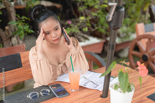 A young Asian woman dines in an al fresco restaurant and is stressed to hear a bad news from her client on the phone.