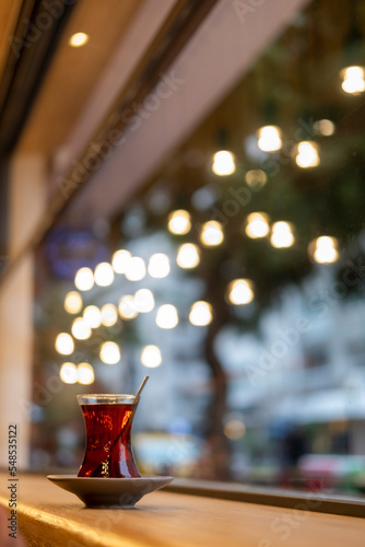 side view of a turkish tea glass and spoon in red tea  yellow warm lights in bokeh effect on background