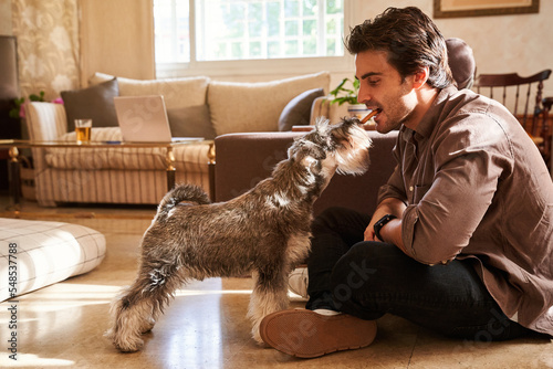Man eating biscuit with dog in living room photo