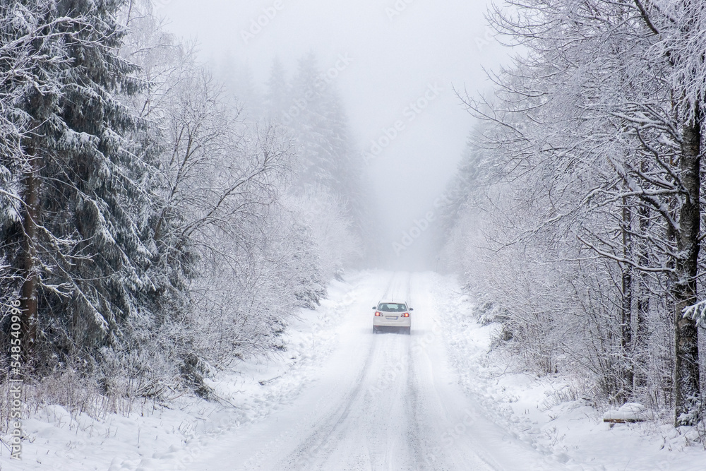 Fototapeta premium Car driving on a slippery road in a winter forest