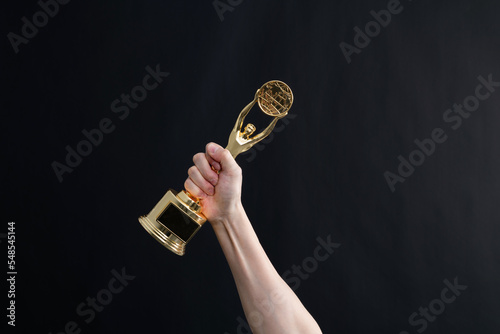 Hand holding golden statuette trophy on black background