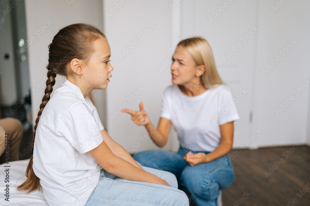 Upset pretty little girl feeling sad sitting side to angry strict blonde mother scolding lecturing difficult kid for bad behavior at home. Mad mom arguing shouting at stubborn child preteen daughter. Upset pretty little girl feeling sad sitting side to angry strict blonde mother scolding lecturing difficult kid for bad behavior at home. Mad mom arguing shouting at stubborn child preteen daughter.