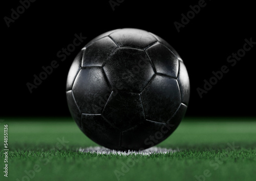 Worn and scratched black leather football on penalty spot, with plain black background. Green grass, astroturf. Football world cup. © Ian