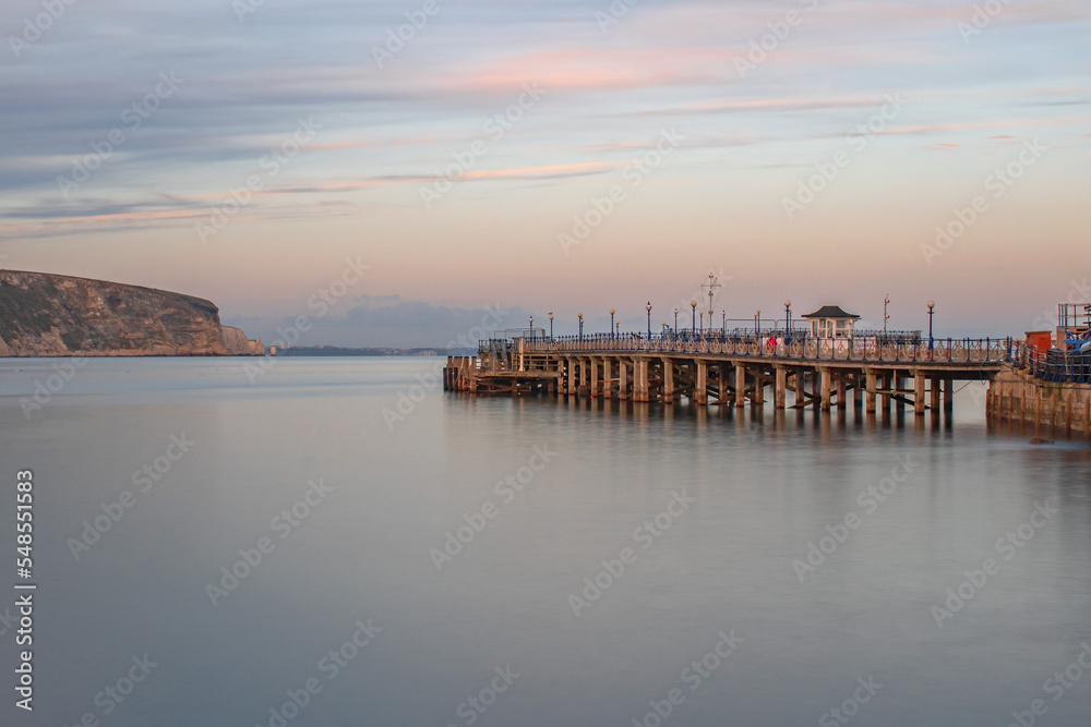 Obraz premium A clear November evening long exposure looking across smooth waters along Swanage Pier with a pink sky