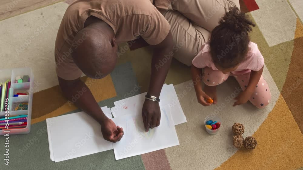 Top view of African American father with little daughter drawing together with crayons sitting on carpet at home Top view of African American father with little daughter drawing together with crayons sitting on carpet at home