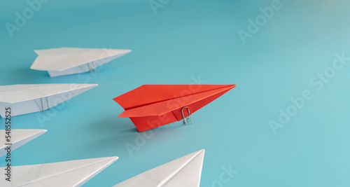 Red paper plane leading a white paper plane on a blue background.