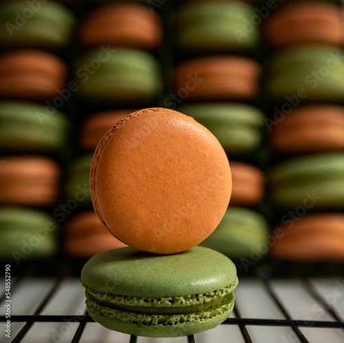 Close-up view of orange and green sweet French macarons on the baking rack