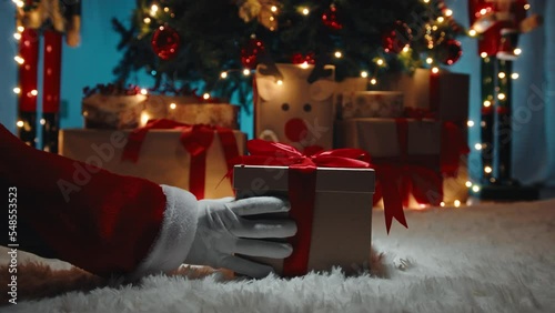 Hand of Santa Claus i deliver the Christmas gift box under the tree 