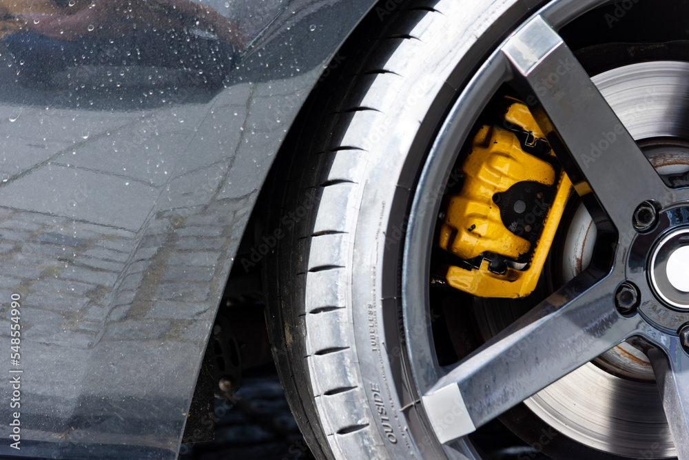 Close up to a black racing car wheel with brake disk and yellow caliper