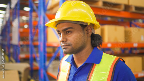 Portrait of Indian worker working in large warehouse retail store industry. Rack of stock storage. Interior of cargo in ecommerce and logistic concept. Depot. People lifestyle. Shipment service. © tampatra