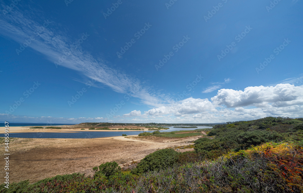 Landscape of Melides, Portugal on hot, summer day. Showing blue sky, bushes and lake meeting sea.