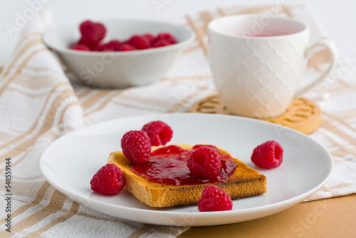 Toast with raspberry jam and cup of tea on beige table.