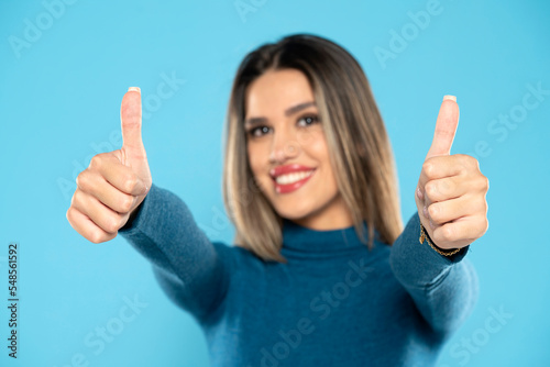 Happy young woman showing thumbs up sign on a blue background © vladimirfloyd