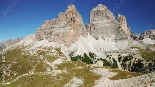 Man and woman stand on hill top edge near gorge looking at majestic mountains. Wide green valleys with paths around Tre Cime di Lavaredo aerial view photo