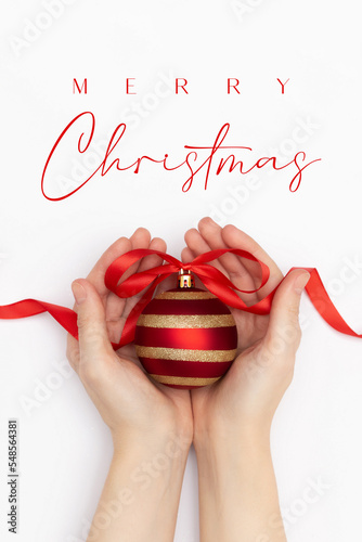Flat lay of female hands holding red and gold christmas ball with red ribbon