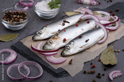 Fotografie Close-up top view of several pickled herrings with spices on parchment paper on a serving board
