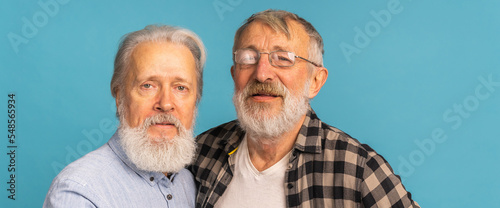 Banner portrait two elderly man friends standing over blue background - friendship, aged and senior people