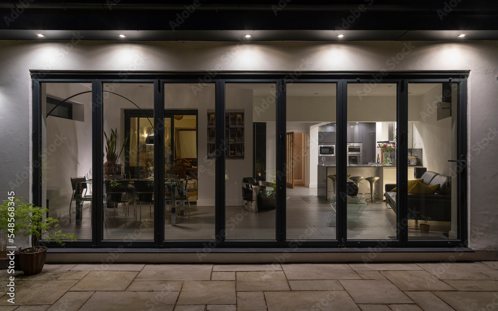 Stylish, bifold doors at night with downlighters revealing interior of a designer, lifestyle, kitchen diner room.