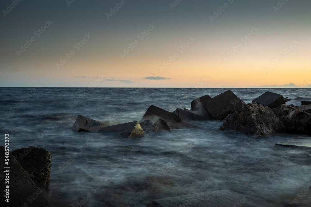 Long exposure image of dramatic sky seascape with rock in sunset scenery background