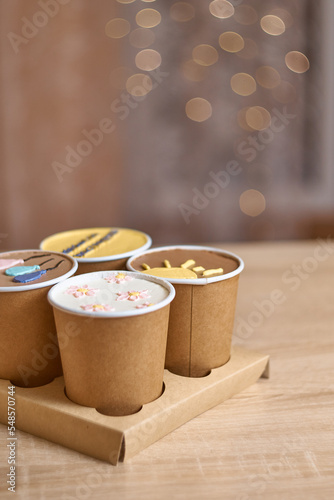four homemade mini chocolate cake to go in coffee cup with cream drawing on a table, confectionery trend concept. Paper cups with cakey are in a box. fashionable dessert. Vertical, copy space, Bokeh