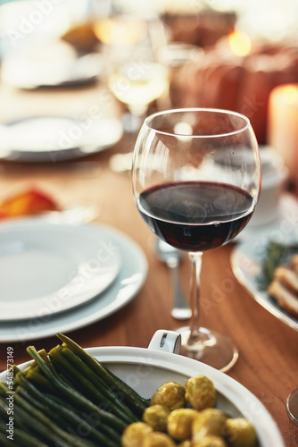 Closeup, glass and wine on table at dinner, restaurant or house for celebration, holiday or party. Red wine, alcohol and vegetables in dining room for thanksgiving, Christmas or fine dining in home